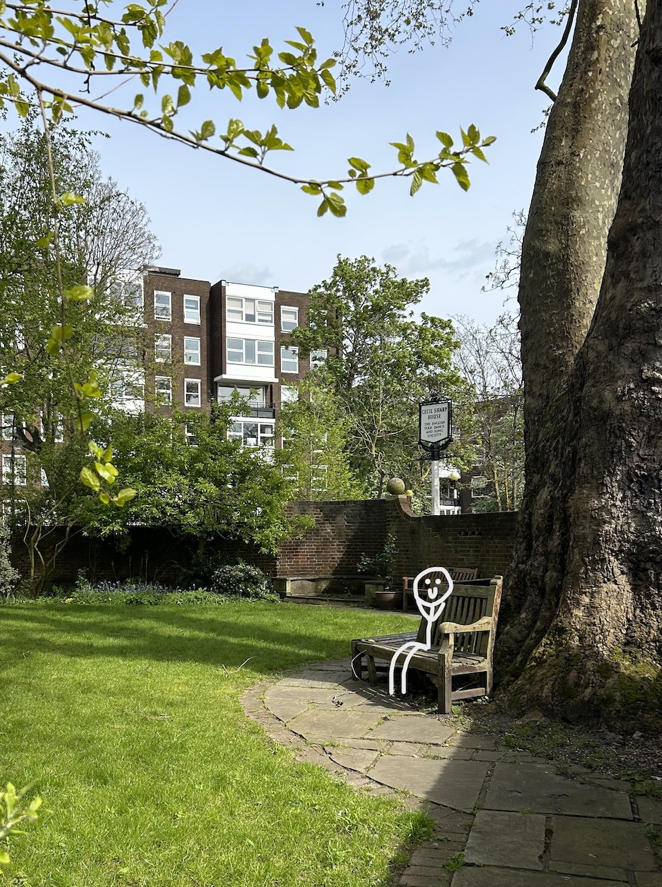 A stick figure sitting on a bench in the garden at Cecil Sharp House